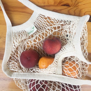 white crochet grocery bag on a table with nectarines and oranges inside