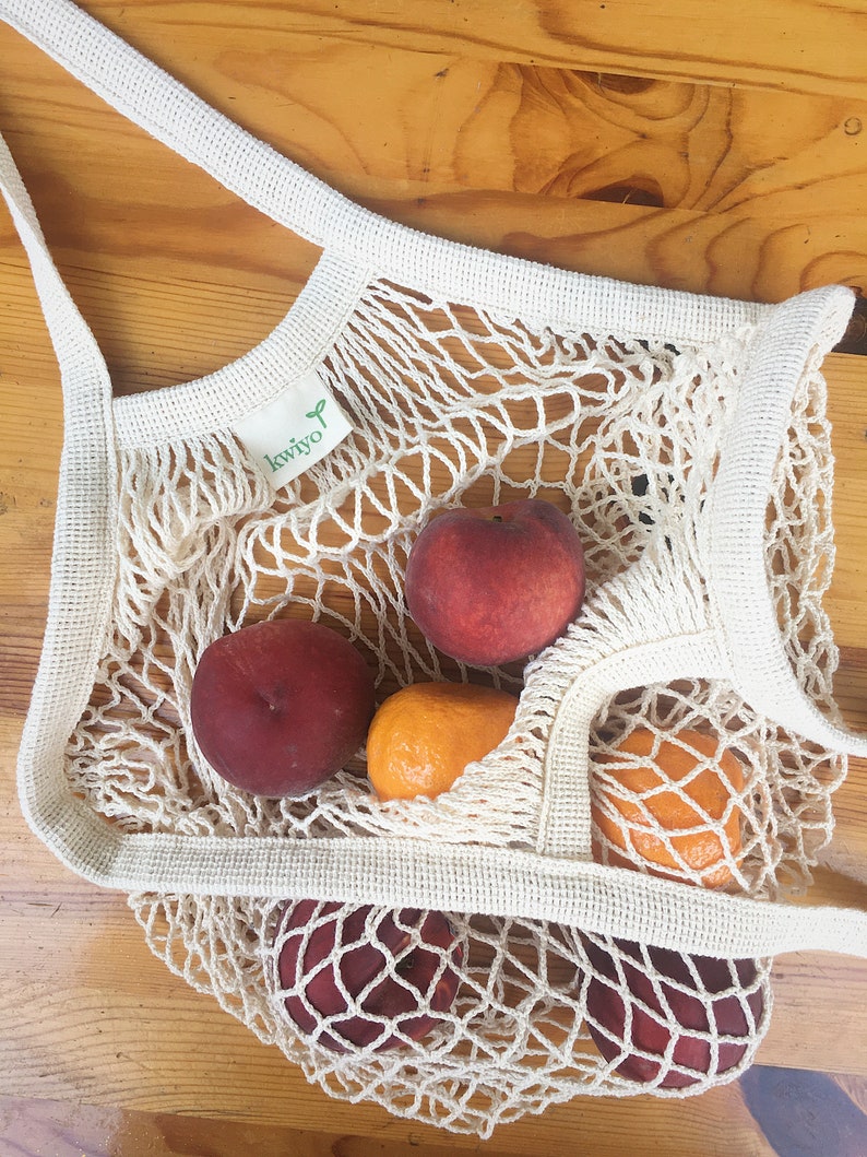 white crochet grocery bag on a table with nectarines and oranges inside