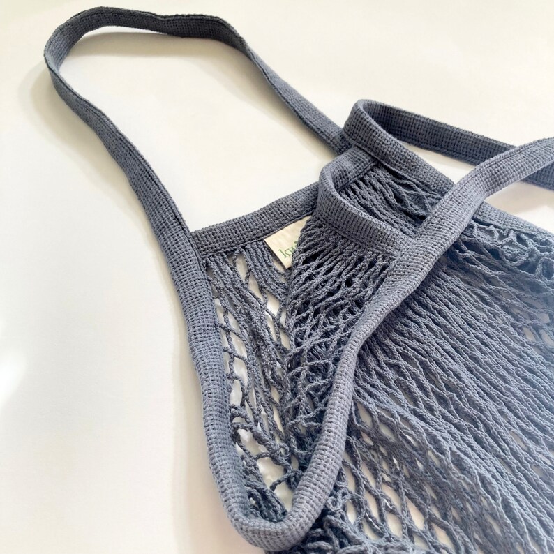 A gray reusable mesh shopping bag with a thick, woven strap. The bag is made of a fine, tightly woven mesh material.