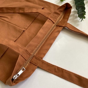Brown work tote bag with zipper and pockets and shoulder straps.