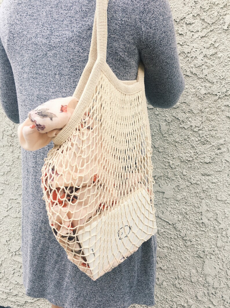 lady wearing on her shoulder a beige cotton mesh bag with planner & scarf inside the bag