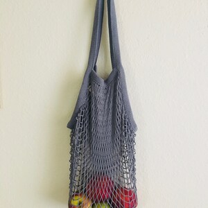 Reusable gray string mesh bag with red and green apples inside. Net tote bag for farmers market produce.