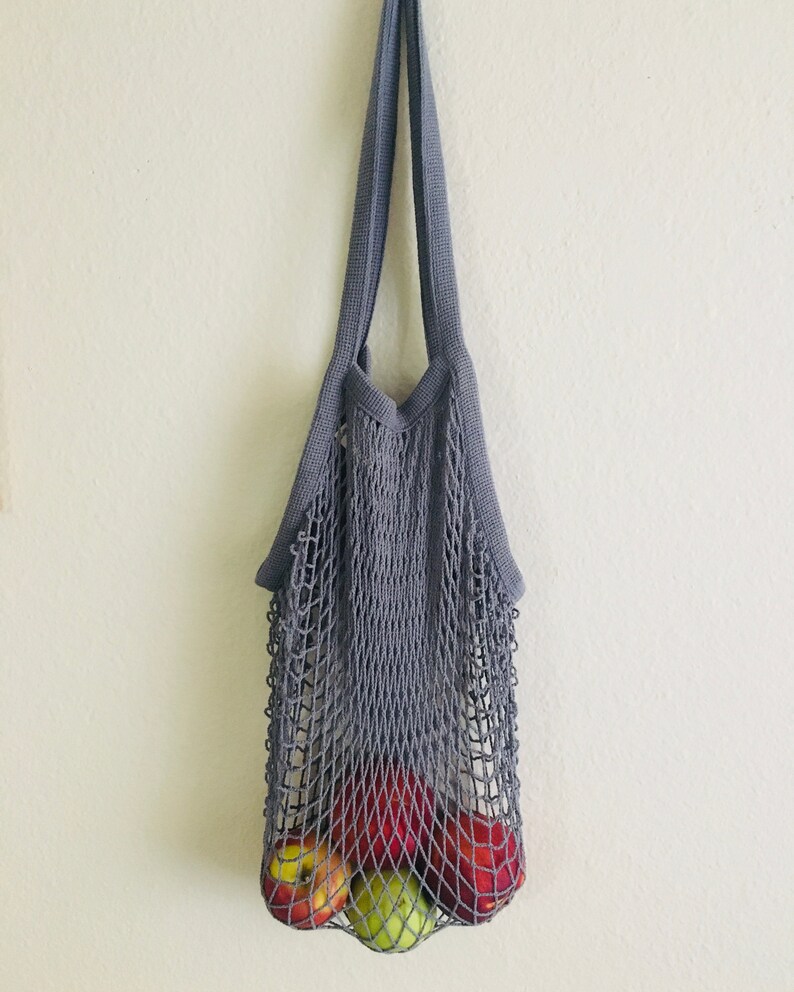 Reusable gray string mesh bag with red and green apples inside. Net tote bag for farmers market produce.