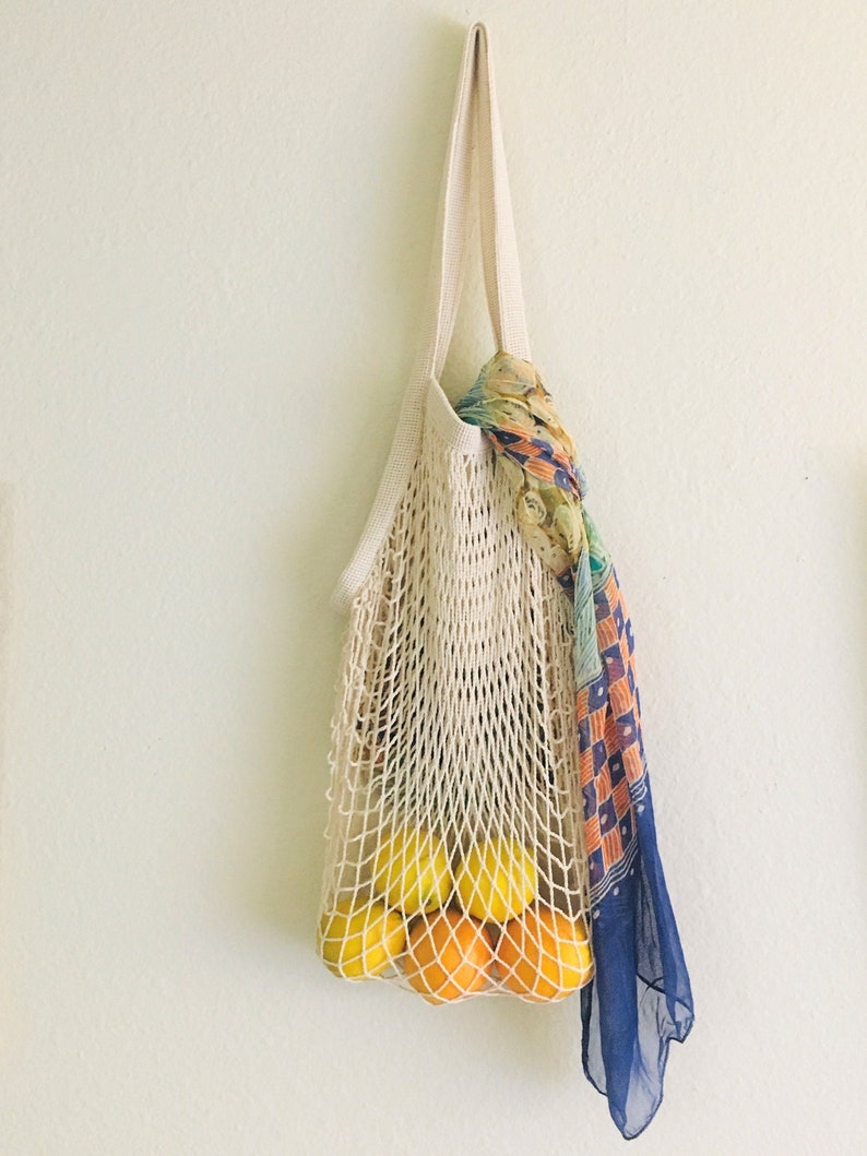 beige market bag with scarf tied around the straps and fruits inside hanging on white wall