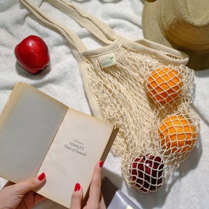 farmers market bag on a blanket with fruits inside. image showing woman's hand holding a book