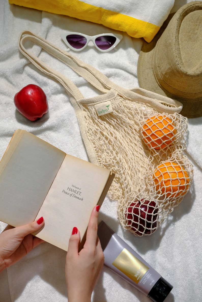 farmers market bag on a blanket with fruits inside. image showing woman's hand holding a book