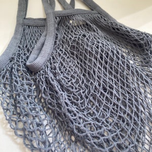 Set of gray string mesh bag with long durable handles. The reusable bag is made of a fine, tightly woven mesh that expands.