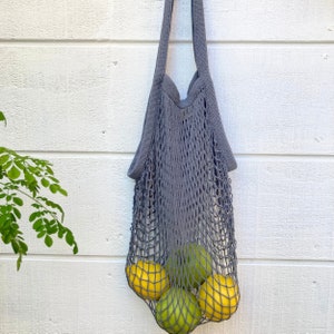 A gray string mesh bag with four fruits inside. The fruits are yellow lemons and green limes. Net tote is versatile and can also be used for storage, beach, picnic, or travel.