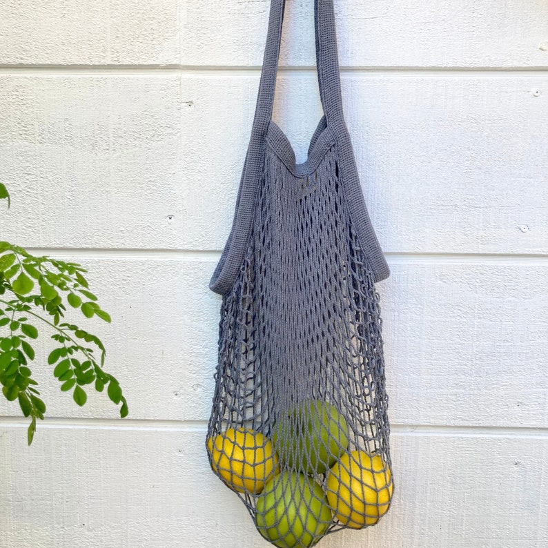A gray string mesh bag with four fruits inside. The fruits are yellow lemons and green limes. Net tote is versatile and can also be used for storage, beach, picnic, or travel.