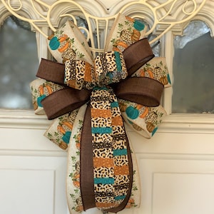 May include: A brown, teal, and orange patterned bow with a brown ribbon. The bow is tied with a loop and is hanging on a white door.