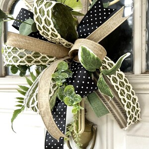 May include: A decorative bow featuring a mix of black and white polka dot ribbon, natural burlap ribbon, and green ribbon with a white lattice pattern. The arrangement includes artificial green eucalyptus leaves and a lime green butterfly accent.