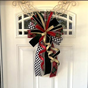 May include: A decorative bow made of multiple ribbons featuring black and white checkered patterns, red and green plaid, solid black velvet, and shimmering gold fabric. The ribbons are arranged in a large, multi-layered cluster with long, curling tails.