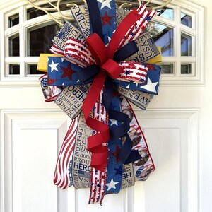 May include: A patriotic door bow featuring red, white, and blue ribbons with star and stripe patterns. The bow includes ribbons with text such as "USA", "Freedom", and "Hero". A decorative accent for Independence Day or other patriotic holidays.