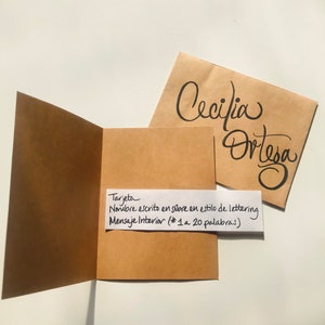 Pu&ograve; includere: Un biglietto marrone con un foglietto bianco attaccato. Il foglietto dice "Tarjeta Nombre escrito en sobre en estilo de lettering Mensaje Interior (* 1 a 20 palabras)". Il biglietto &egrave; aperto e l'interno &egrave; vuoto. Una busta marrone con il nome "Cecilia Ortesa" scritto in corsivo nero &egrave; visibile sullo sfondo.