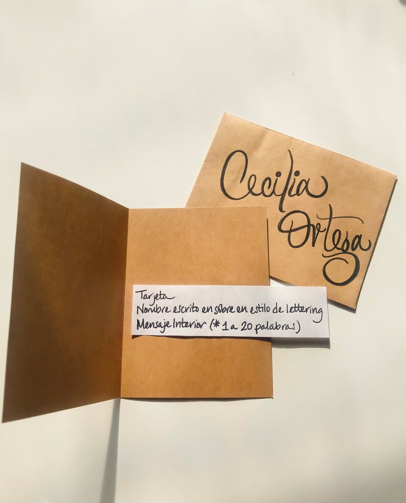 Pu&ograve; includere: Un biglietto marrone con un foglietto bianco attaccato. Il foglietto dice "Tarjeta Nombre escrito en sobre en estilo de lettering Mensaje Interior (* 1 a 20 palabras)". Il biglietto &egrave; aperto e l'interno &egrave; vuoto. Una busta marrone con il nome "Cecilia Ortesa" scritto in corsivo nero &egrave; visibile sullo sfondo.
