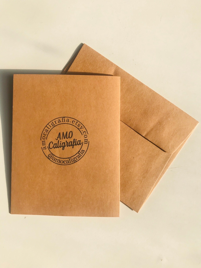 Pu&ograve; includere: Una busta di carta marrone con un logo circolare che dice "AMO Calligrafia" e "amocalligrafia.etsy.com" in testo nero.