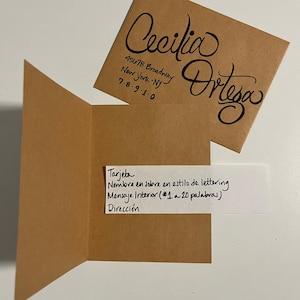 Pu&ograve; includere: Una busta marrone con un biglietto bianco all'interno. La busta ha il nome "Cecilia Ortega" scritto in corsivo sul davanti, insieme a un indirizzo e un numero di telefono. Il biglietto ha il testo "Tarjeta, Nombre en sobre en estilo de lettering, Mensaje Interior (#1 a 20 palabras), Direcci&oacute;n" scritto in inchiostro nero.