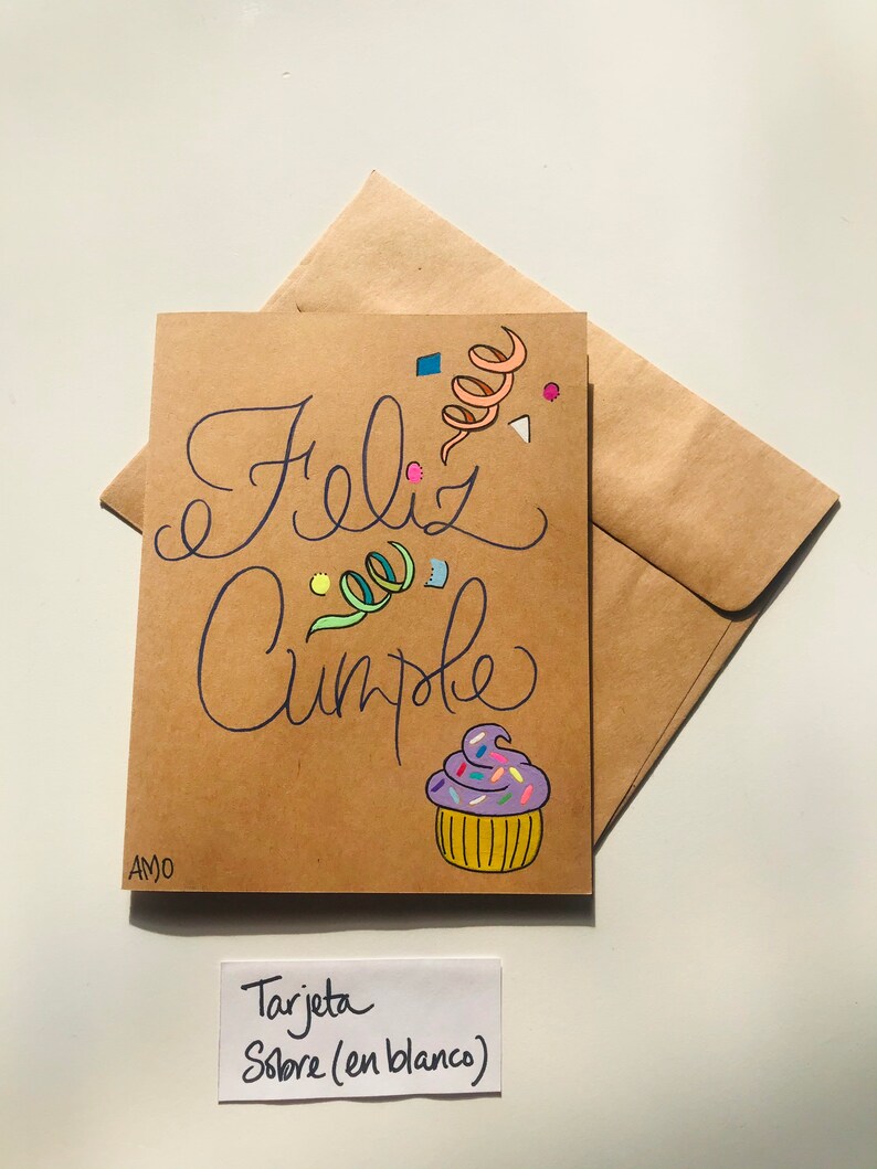 Pu&ograve; includere: Un biglietto marrone con le parole "Feliz Cumple" scritte in corsivo nero. Il biglietto &egrave; decorato con coriandoli colorati e un cupcake viola con codette. Il biglietto &egrave; etichettato "Tarjeta Sobre (en blanco)"