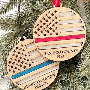 May include: Two wooden Christmas ornaments with an American flag design. One ornament has a red stripe across the flag and the text "Henrico County Fire". The other ornament has a blue stripe across the flag and the text "Henrico County Police".