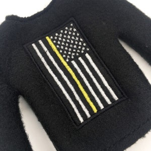 May include: Black long-sleeved shirt with an embroidered American flag patch featuring a yellow stripe.