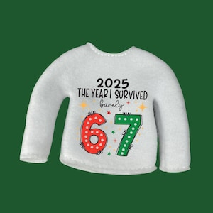 May include: White long-sleeved sweater with the text "2025 THE YEAR I SURVIVED barely" and the numbers "67". The number 6 is red with white polka dots, and the number 7 is green with white polka dots. The sweater has a green background.