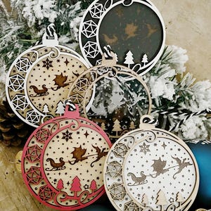 May include: Five wooden Christmas ornaments with a laser-cut design of a dragon pulling a sleigh with a crescent moon and stars. The ornaments are in various colors, including natural wood, black, and red.