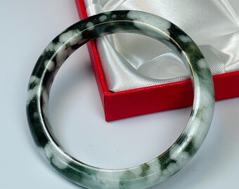 May include: A green and white jade bangle bracelet with a cloudy pattern. The bracelet is in a red box with white satin lining.