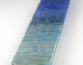 Könnte beinhalten: Ein rechteckiges Glaskunstwerk mit strukturierter Oberfläche. Das Glas geht von einem tiefen Blau oben in ein helleres Blau und Aqua unten über. Das Stück hat eine wellenartige Textur.