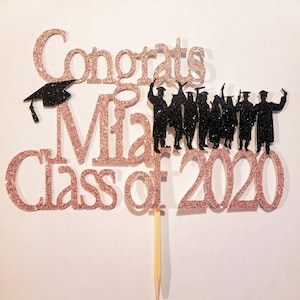Puede incluir: Topper de pastel de purpurina dorada rosa con el texto "Congrats Mia Class of 2020" y una silueta de un grupo de graduados lanzando sus gorros al aire.