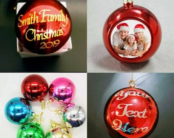 Op de afbeelding: Een set van zes rode, roze, blauwe, groene, zilveren en gouden kerstballen. De ballen zijn rond en glanzend. Eén bal heeft de tekst "Smith Family Christmas 2019" erop. Een andere bal heeft een foto van een gezin van drie. De derde bal heeft de tekst "your text here" erop.