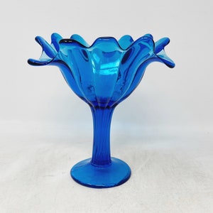 May include: A blue glass bowl with a fluted design and a pedestal base. The bowl is shaped like a flower.