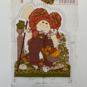 May include: A fabric panel featuring a Cabbage Patch Kid doll illustration. The doll has red hair, brown overalls, and holds a shovel and a basket of vegetables. The panel includes instructions and the text "LEAVE OPEN FOR STUFFING".