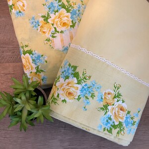 May include: Two yellow pillowcases with a floral pattern. One pillowcase has a white lace trim and a floral pattern with yellow roses and blue forget-me-nots. The other pillowcase has a floral pattern with yellow roses and blue forget-me-nots.
