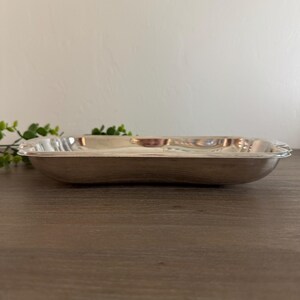 Op de afbeelding: Een rechthoekige zilverkleurige serveerschaal met licht gebogen randen. De schaal heeft een reflecterend oppervlak en is leeg. De schaal staat op een houten oppervlak.