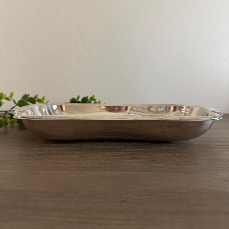 Op de afbeelding: Een rechthoekige zilverkleurige serveerschaal met licht gebogen randen. De schaal heeft een reflecterend oppervlak en is leeg. De schaal staat op een houten oppervlak.