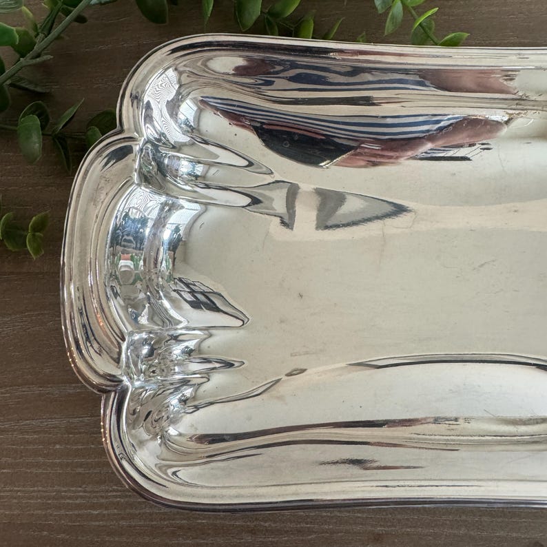 Op de afbeelding: Een rechthoekige, zilverkleurige serveerschaal met een geschulpte rand. Het gepolijste oppervlak reflecteert de omgeving. De schaal is waarschijnlijk van metaal en is bedoeld voor het serveren van voedsel of het presenteren van items.