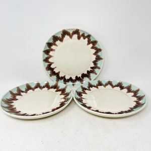 May include: Set of three white ceramic plates with a brown and blue design. The plates have a white center and a brown and blue rim.