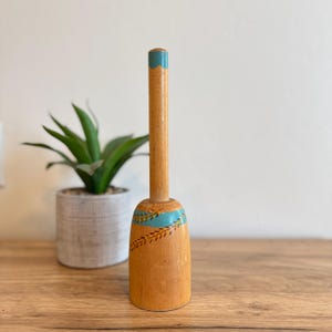 May include: A wooden kitchen utensil with a blue and yellow painted design. The utensil has a long handle and a rounded base.