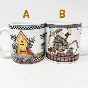 May include: Two white ceramic mugs with Christmas-themed designs. One mug features a birdhouse with a cardinal, while the other mug features Santa Claus on a sleigh.