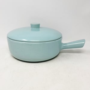 May include: A light blue ceramic casserole dish with a lid and a single handle. The dish is round and has a smooth, glossy finish.