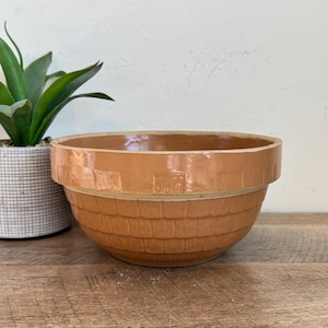 May include: A large, brown ceramic mixing bowl with a basket weave pattern. The bowl has a slightly glazed finish and a wide rim.