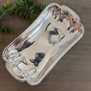 Op de afbeelding: Een rechthoekige, zilverkleurige serveerschaal met een geschulpte rand. De schaal heeft een reflecterend oppervlak en de randen zijn iets verhoogd. De schaal is leeg en ligt op een houten oppervlak.