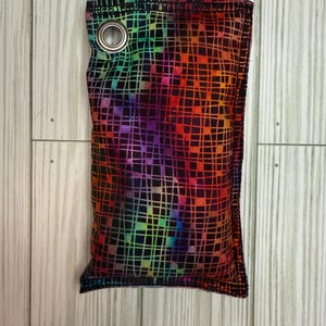 May include: A rectangular fabric item with a vibrant, multicolored grid pattern, featuring a spectrum of colors from red to purple. It has a metal grommet at the top and appears to be a small bag or pouch.