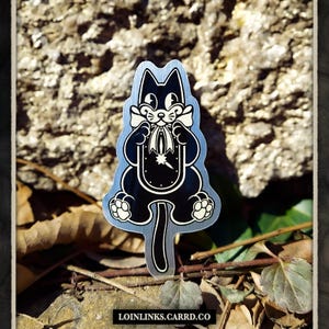 May include: A black and white metal sticker of a cat holding a clock with a star on it. The cat is wearing a bow tie and has a long tail.