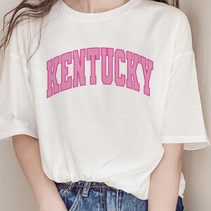 May include: White t-shirt with a pink "KENTUCKY" graphic in an arched font.
