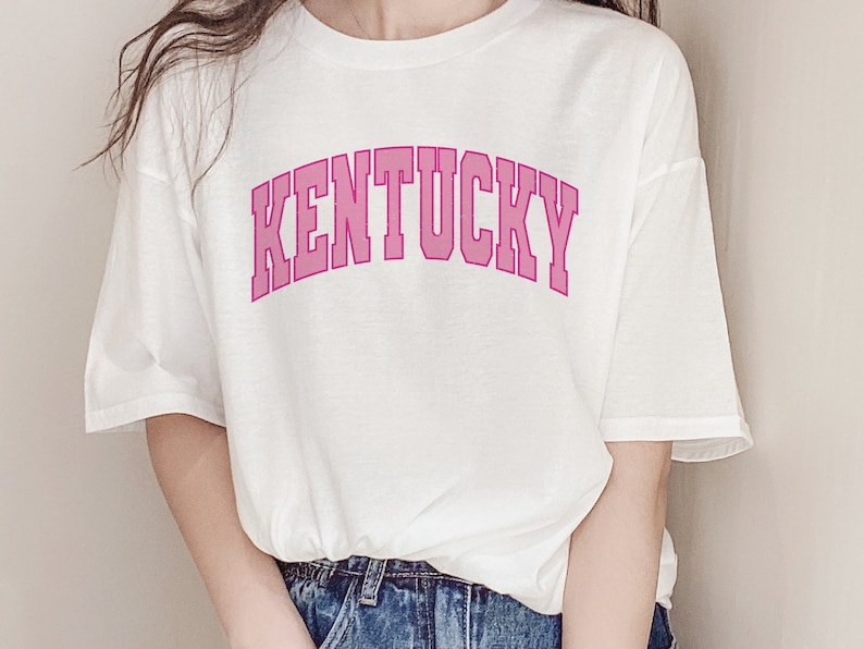 May include: White t-shirt with a pink "KENTUCKY" graphic in an arched font.