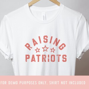 May include: White t-shirt with a red distressed graphic that says "Raising Patriots" with three stars.