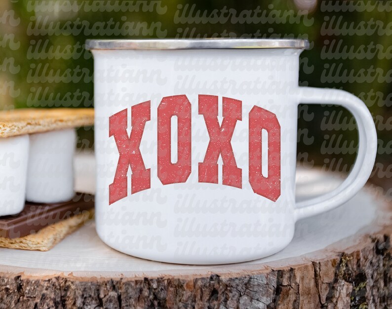 May include: White enamel camping mug with a red XOXO graphic. The mug is sitting on a wooden surface.