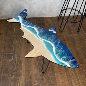 May include: A wooden coffee table shaped like a shark with a blue and white resin ocean wave design.
