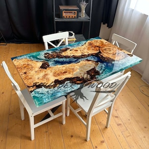 May include: A rectangular wooden table with a clear epoxy resin top, featuring a design of brown wood and blue resin. The table is surrounded by four white chairs. The table measures approximately 60 inches long.